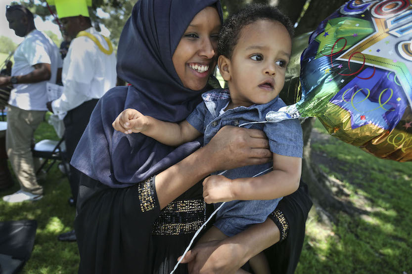 Anisa Omar holds her friend’s son while his mother dances at a picnic where primarily Congolese refugees celebrate completion of English classes. (Photo by Peggy Peattie for CALmatters)