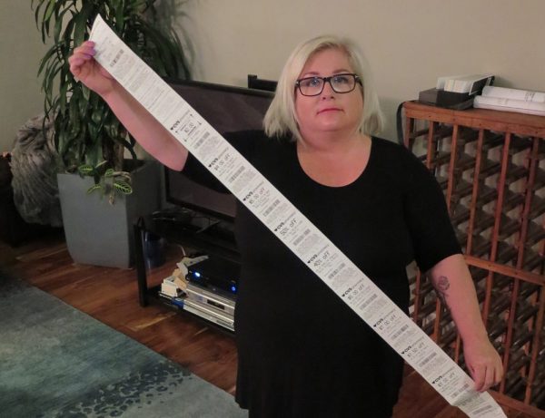 Carol Dahmen poses with a receipt that’s more than 4 feet long—for the purchase of a single item. (Photo via Kevin Eckery for CALmatters)
