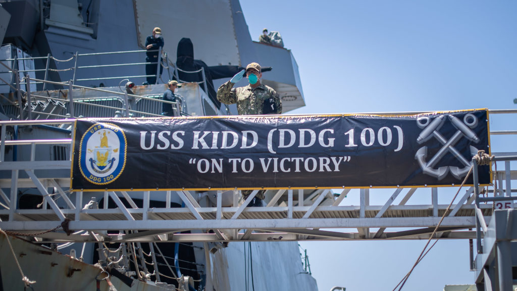 A sailor salutes the national ensign as he disembarks the guided-missile destroyer USS Kidd at Naval Base San Diego on Tuesday as part of the Navy’s aggressive response to the COVID-19 outbreak on board the ship. While in San Diego, the Navy will provide medical care for the crew and clean and disinfect the ship. (U.S. Navy photo by Mass Communication Specialist 2nd Class Alex Corona)